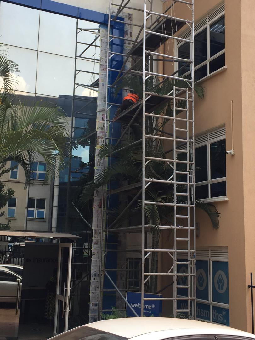 Painter accessing an upper floor of a glass-facade office building via aluminium tower scaffold