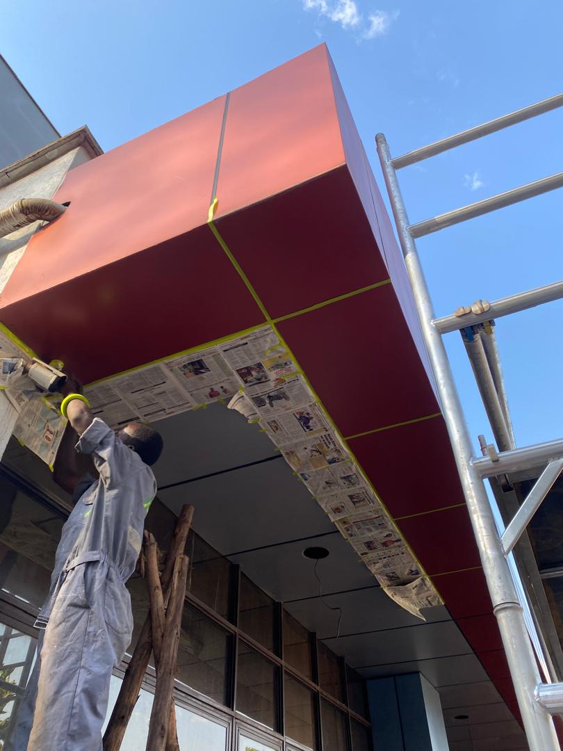 Painter masking the underside of a commercial entrance canopy before the finishing coat