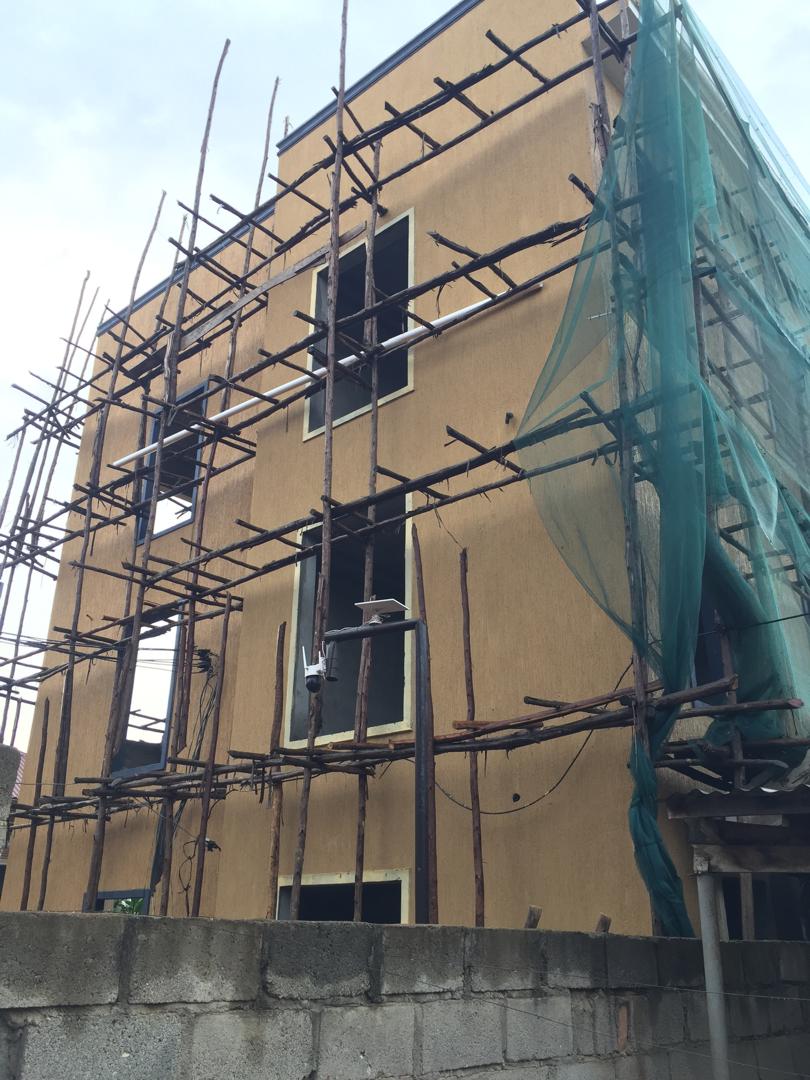 Full height view of a scaffolded commercial building mid-repaint with a gold render finish