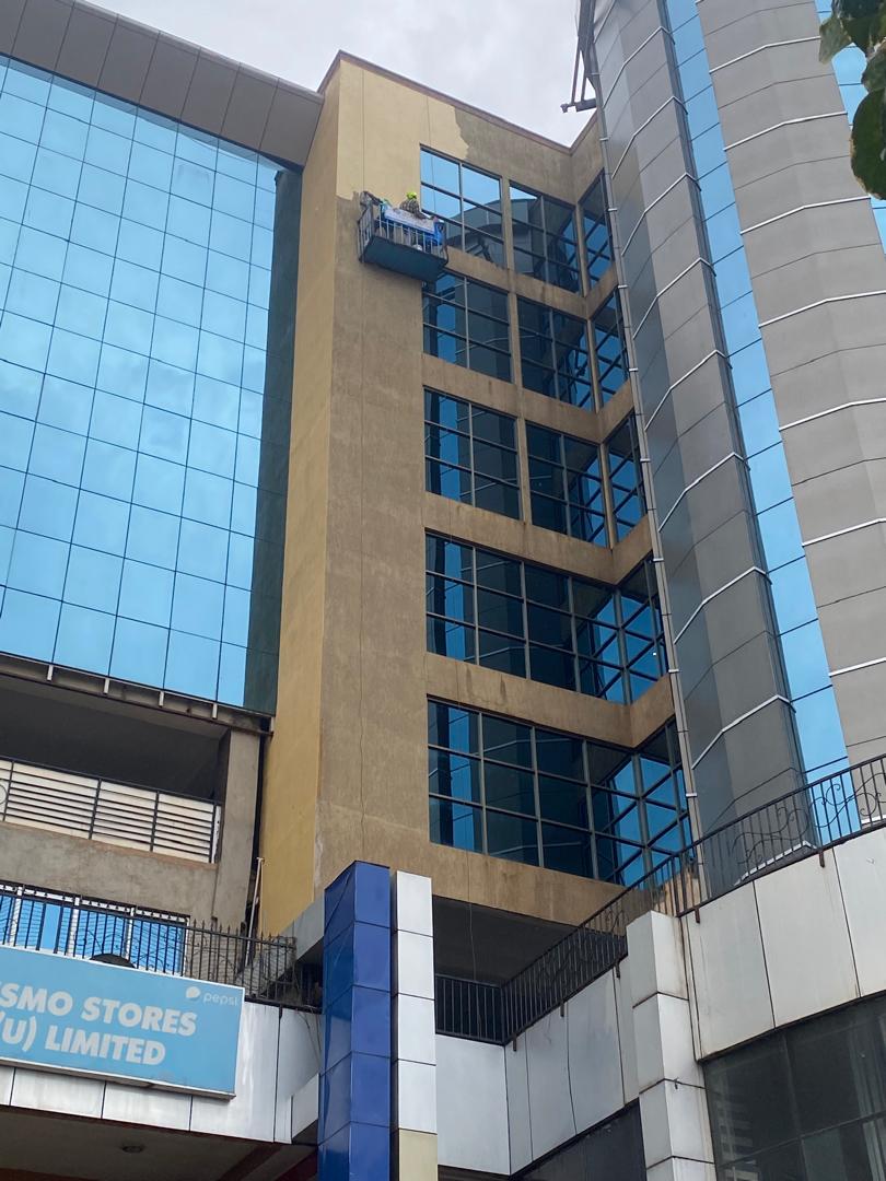Painter on a suspended cradle repainting the upper floors of a glass high-rise facade
