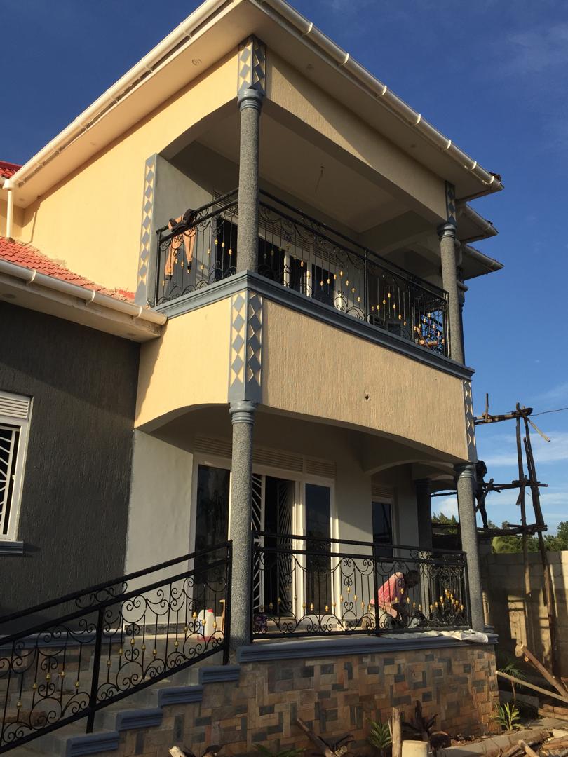 Two-storey residence exterior with diamond-pattern pillar trim and wrought iron balconies under construction