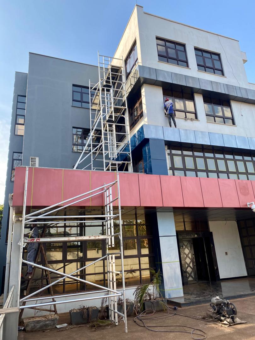 Two-storey gabled residence in yellow render with brick pillar accents, painter on scaffold