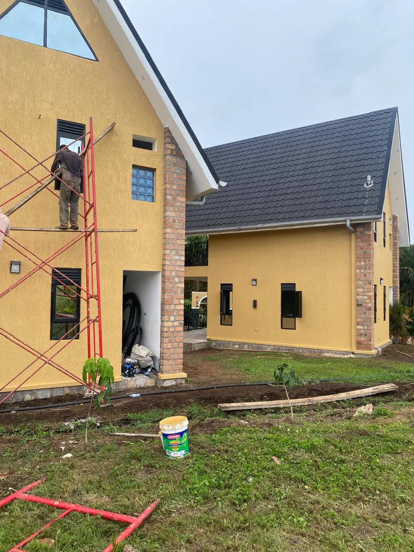 Painter on mobile scaffold finishing the upper storey of a yellow gabled residence