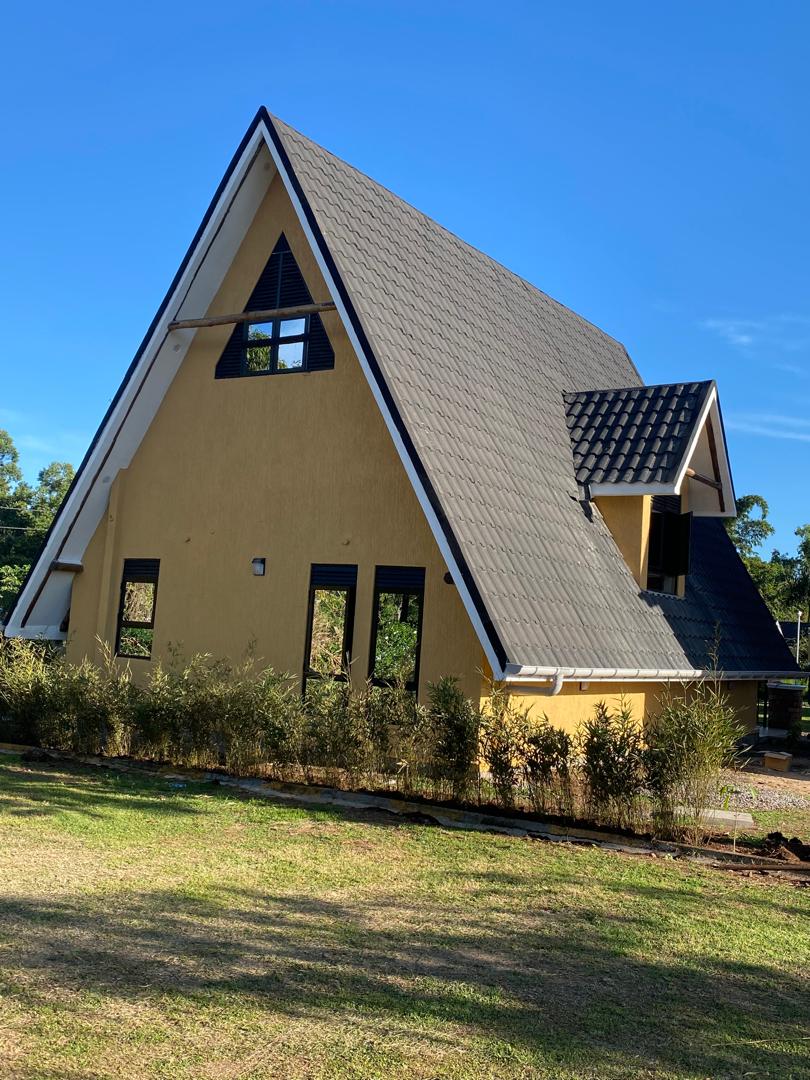 Full elevation of a yellow A-frame chalet with a steep dark tiled roof under a clear sky