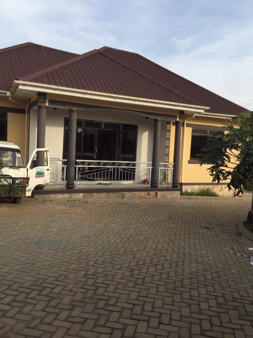 Single-storey bungalow exterior with sand-textured render and gold-trimmed window cornices, Kampala